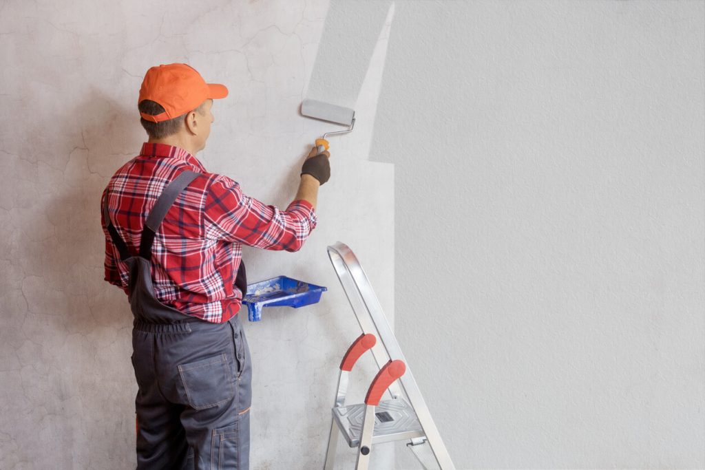 Painter painting a wall with paint roller.