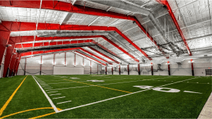 Commercial interior painting completed inside the Spring Lake Fieldhouse featuring red structural joists, white dry fall ceilings, exposed overhead systems, and indoor turf training field.