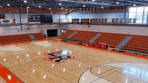 Elk Rapids High School main gymnasium with exposed steel joist ceiling and orange school-branded block walls, painted by Vork Brothers Painting Nort