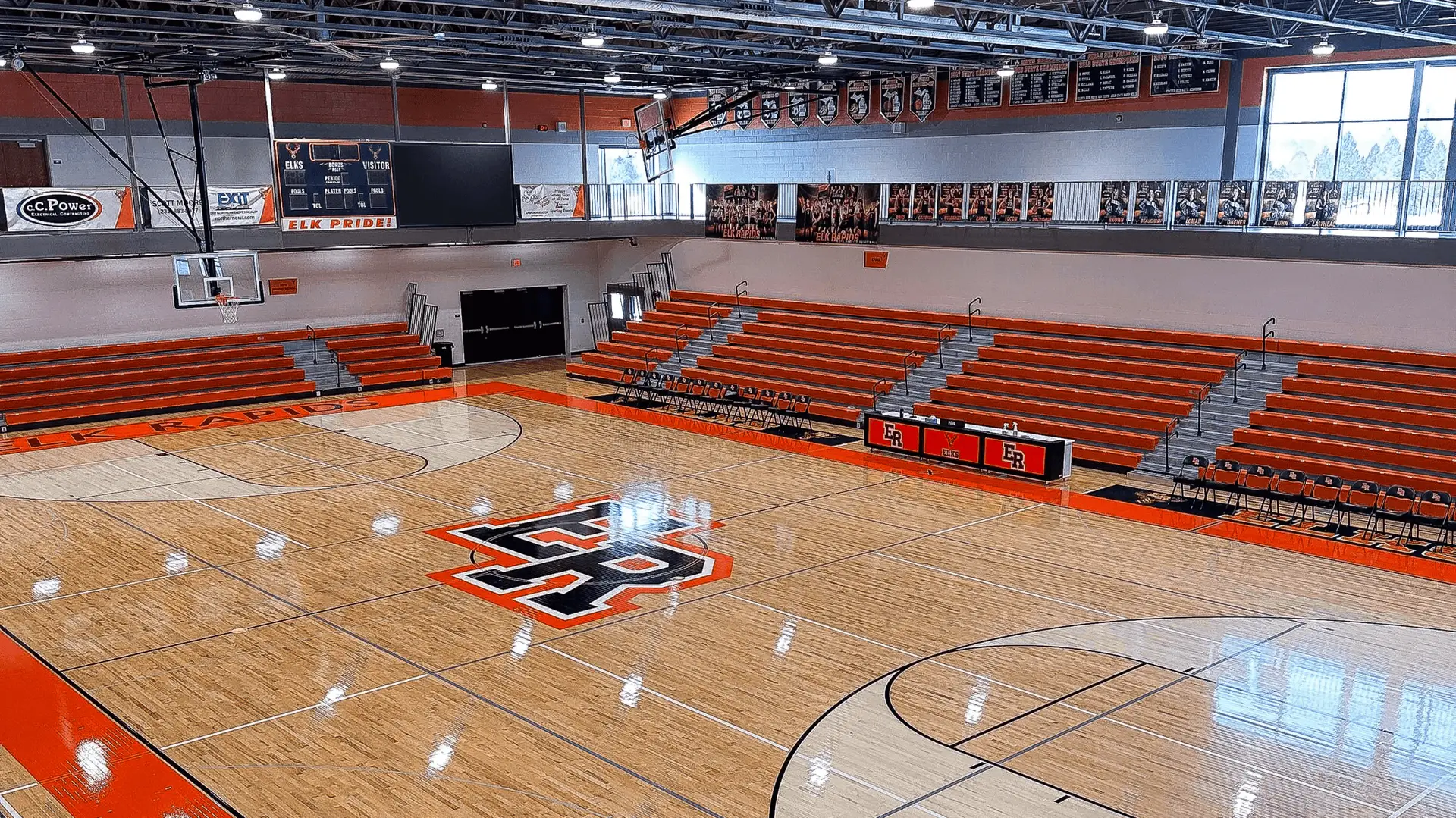 Elk Rapids High School main gymnasium with exposed steel joist ceiling and orange school-branded block walls, painted by Vork Brothers Painting Nort